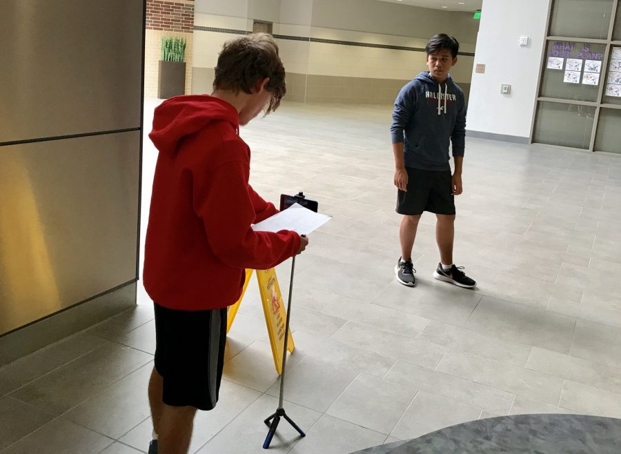 Two students shoot their first project in Digital video and Audio design. Before, students had learned the necessary basics to create the project.  Student to the front left uses their screenplay for reference while recording. Student to the back right acts out the scene in front of the camera. 