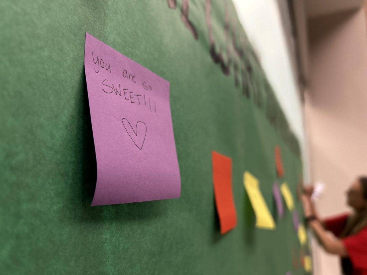 Teacher writes a kind message on the Cain Student Council Stinky Note Board for someone to take